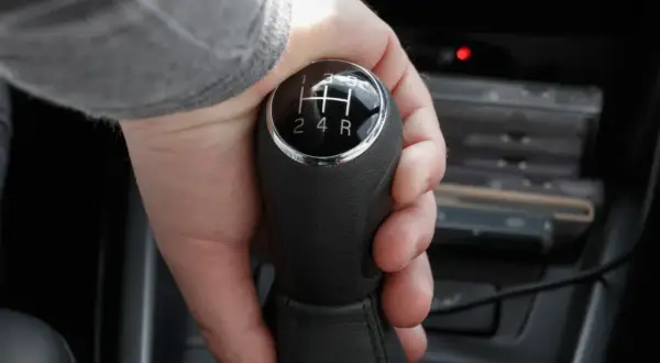 Dłoń chwyta lewarek zmiany biegów, ustawiając go na wsteczny w automacie.