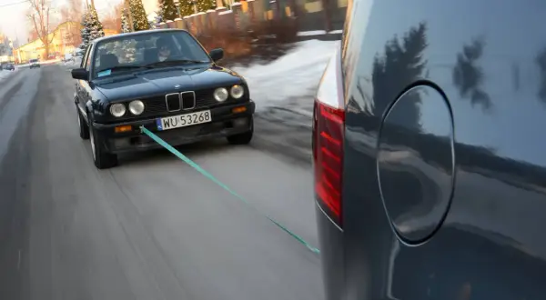 Czarny BMW holowany przez inny samochód, bo zabrakło paliwa. Co zamiast plaka do odpalenia? Lina holownicza!