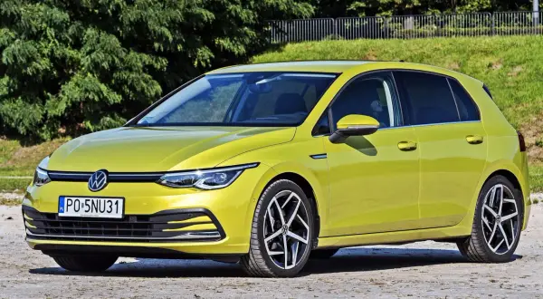 Żółty Volkswagen Golf 8, jeden z wielu popularnych **volkswagen nazwy modeli**, zaparkowany na tle zieleni.