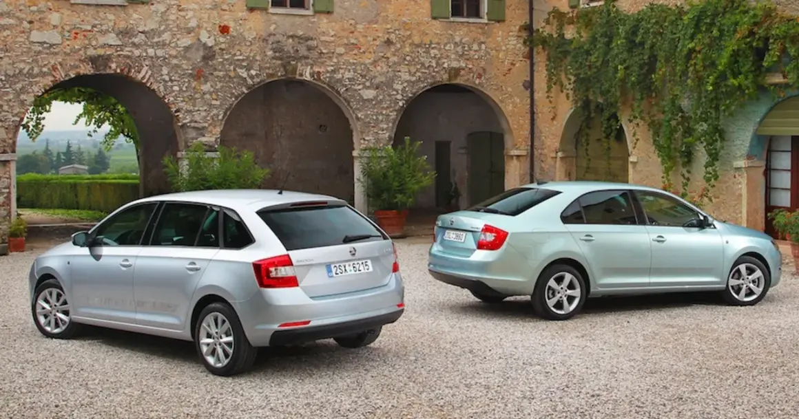 Dwa samochody: srebrny liftback i błękitny hatchback, stoją przed kamiennym budynkiem z łukami i zielenią.
