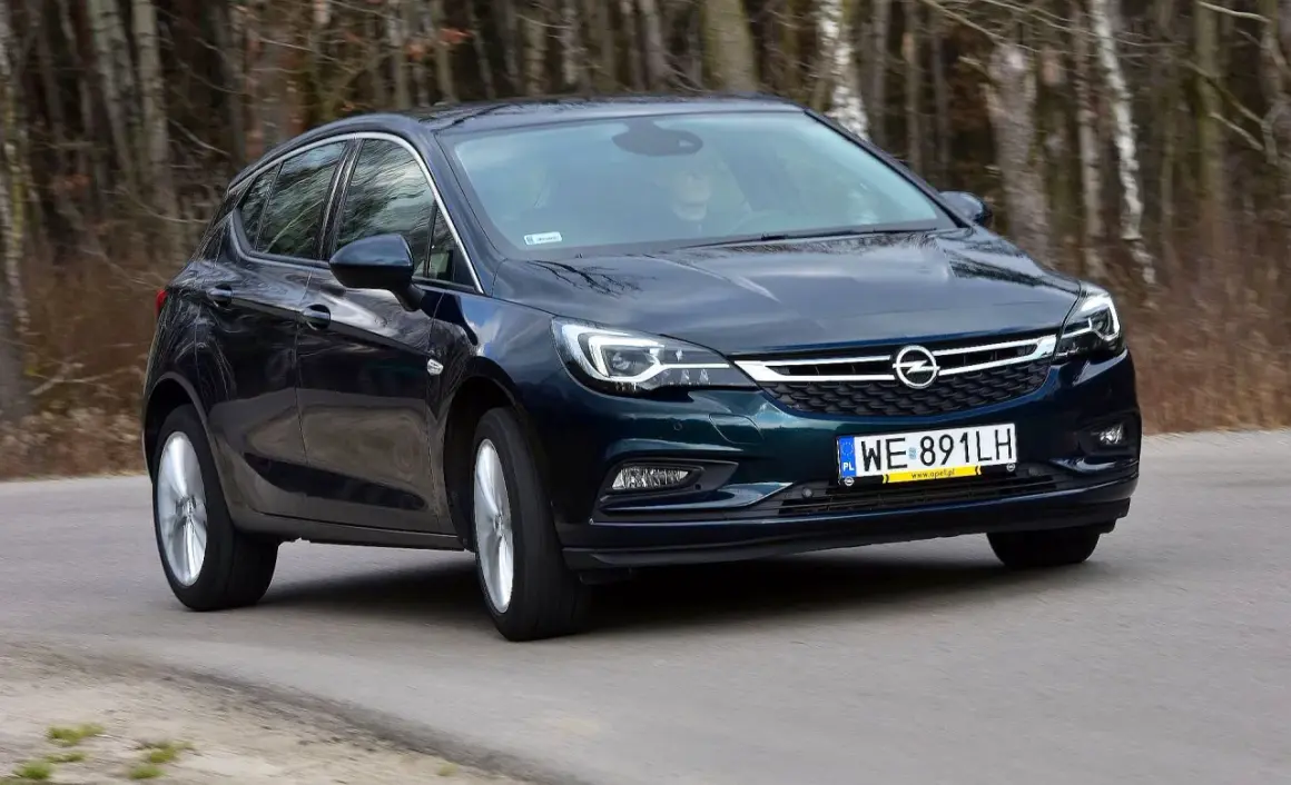 Ciemnozielona Astra K 1.6 CDTI w ruchu, z widocznym kierowcą za kierownicą, na tle lasu.