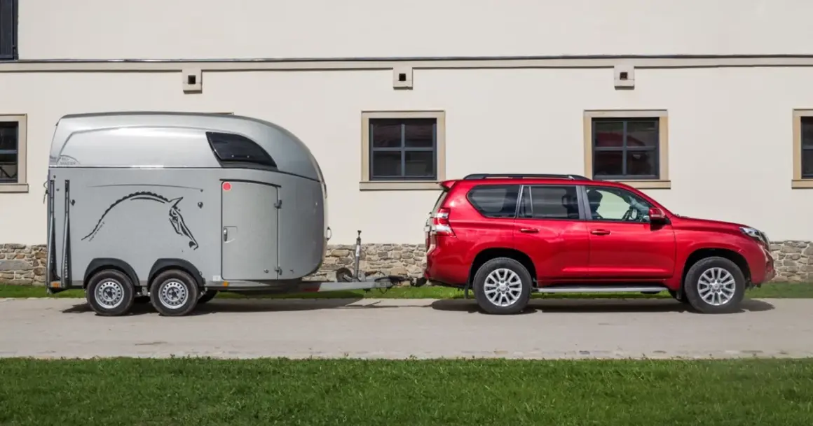 Czerwony SUV holuje przyczepę z koniem. B+E co daje? Możliwość przewiezienia ukochanego zwierzęcia w komfortowych warunkach.