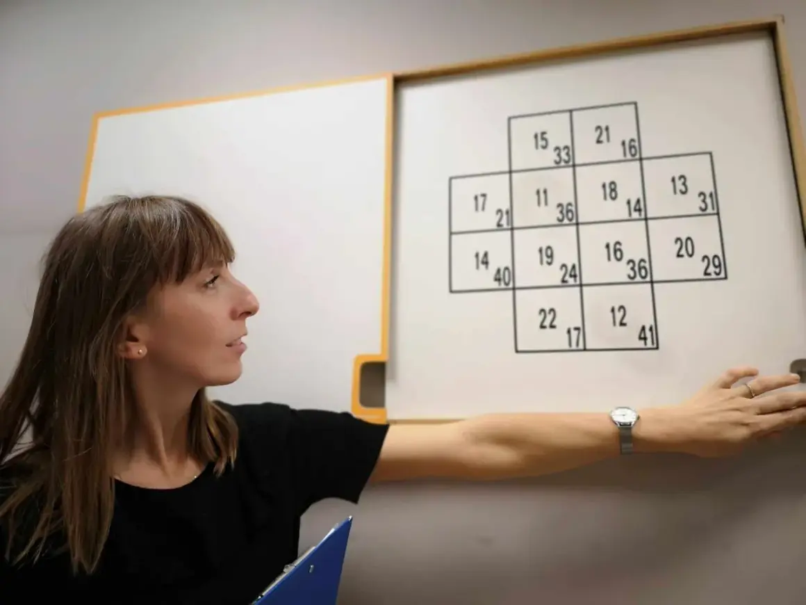 Kobieta podczas testów psychologicznych dla kierowców, wskazująca na tablicę z liczbami.