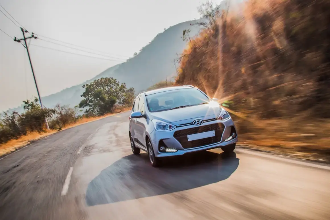 Srebrny Hyundai przemierza krętą drogę w słoneczny dzień. Ten Hyundai z jakiego kraju pochodzi? Z Korei Południowej, gdzie powstała ta marka.