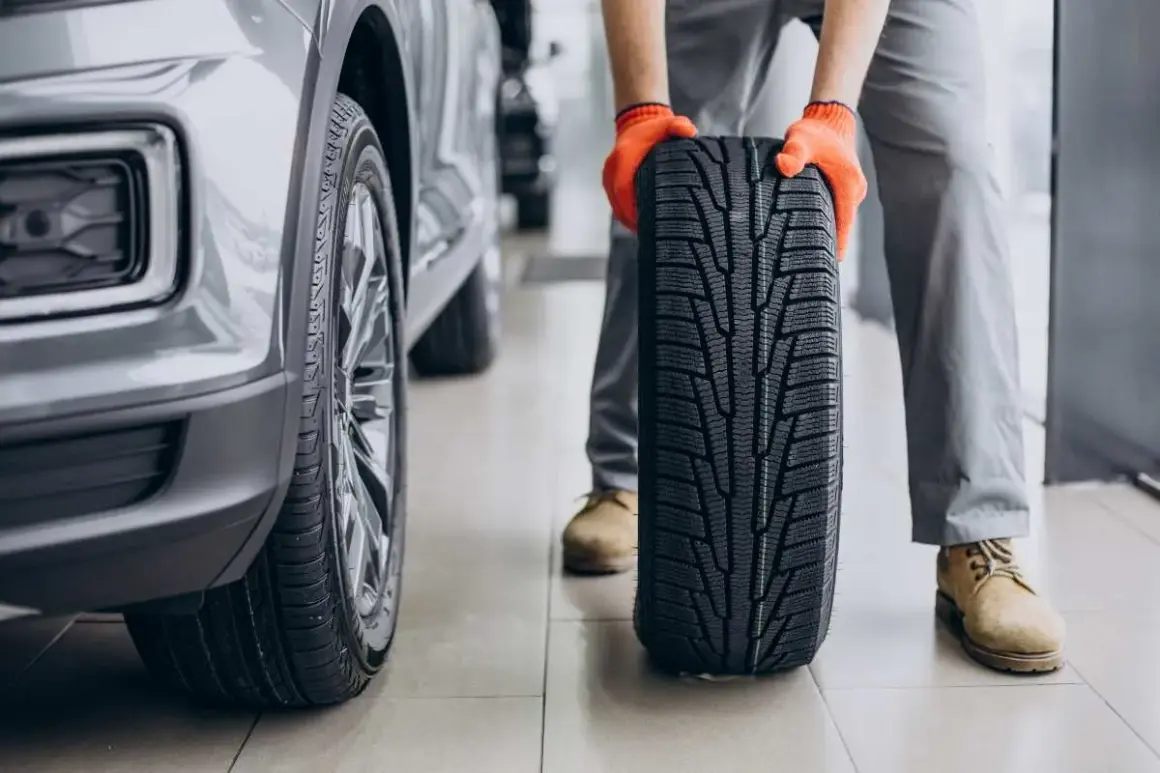 Mechanik w pomarańczowych rękawiczkach trzyma nowe opony letnie obok samochodu. Czas na test opon letnich!