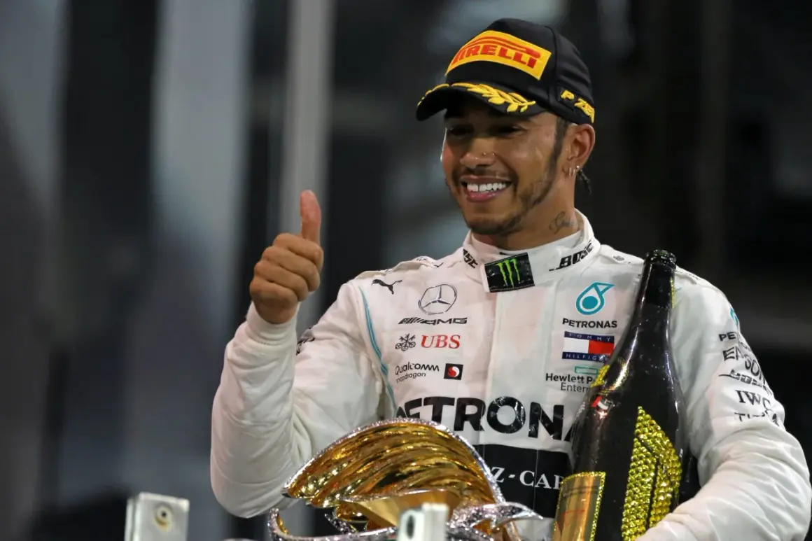 Lewis Hamilton, jeden z najlepsi kierowcy f1, świętuje zwycięstwo z pucharem i szampanem, pokazując kciuk w górę.