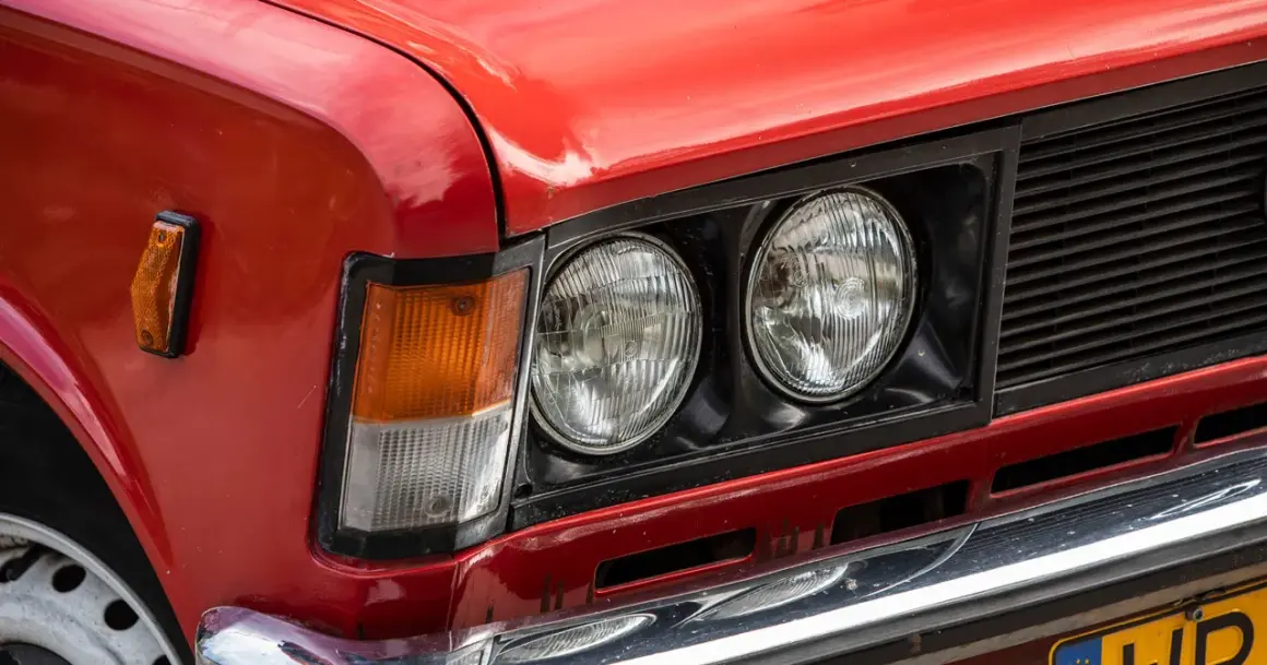Czerwone auto z włoch, z podwójnymi okrągłymi reflektorami i pomarańczowym kierunkowskazem.