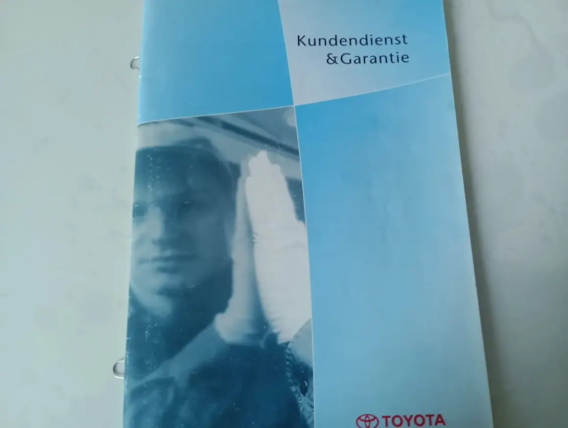 Karta serwisowa pojazdu Toyota z napisem "Kundendienst & Garantie". Widoczny fragment twarzy mechanika w białej rękawiczce.