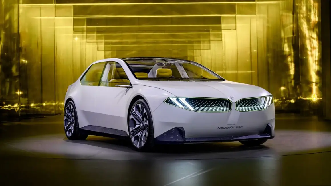 Biały koncept BMW Neue Klasse z futurystycznymi światłami i żółtym wnętrzem, prezentowany na tle złotej, lśniącej ściany.