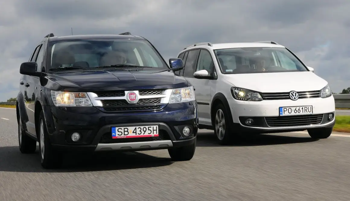 Dwa duże samochody rodzinne, ciemny Fiat i biały Volkswagen, jadą obok siebie po drodze.