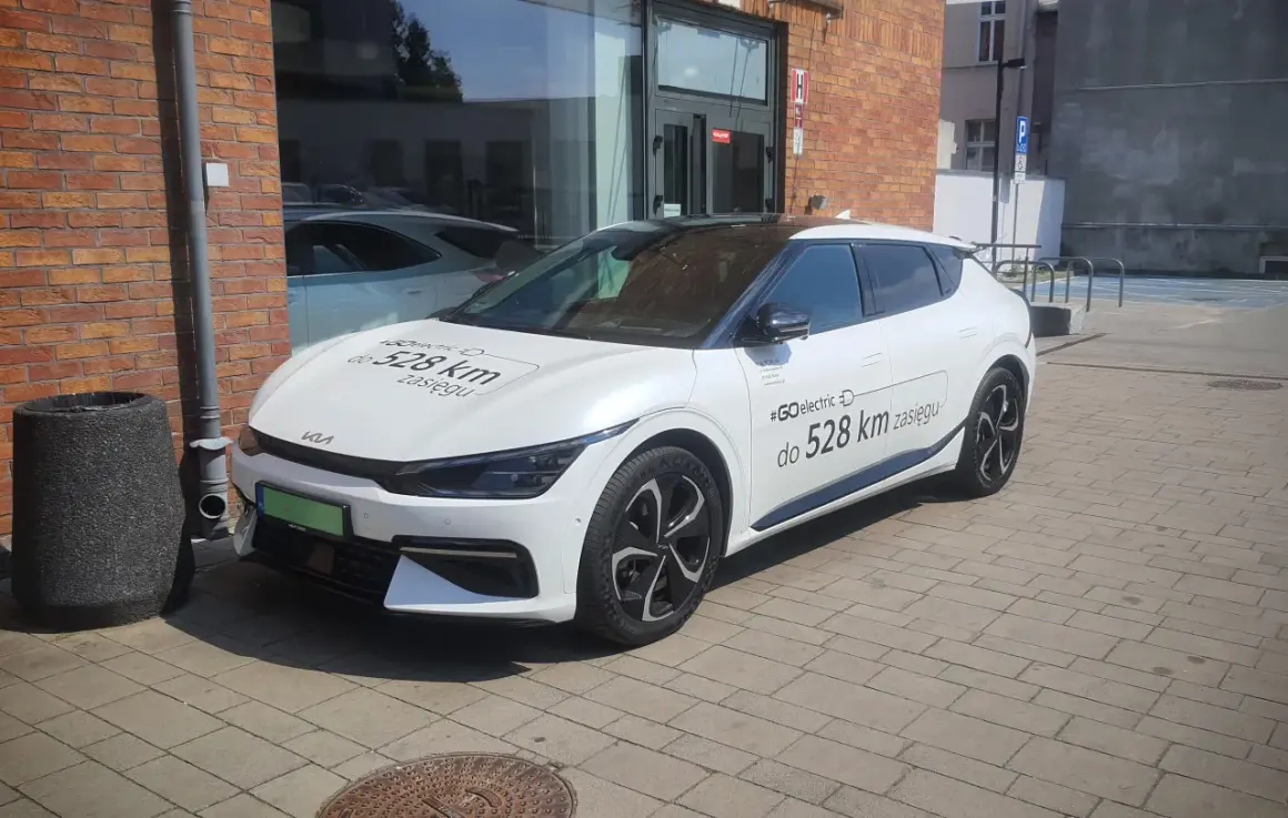 Biały samochód elektryczny Kia z napisem "#GOelectric D do 528 km zasięgu" informuje, ile prądu zużywa samochód elektryczny.