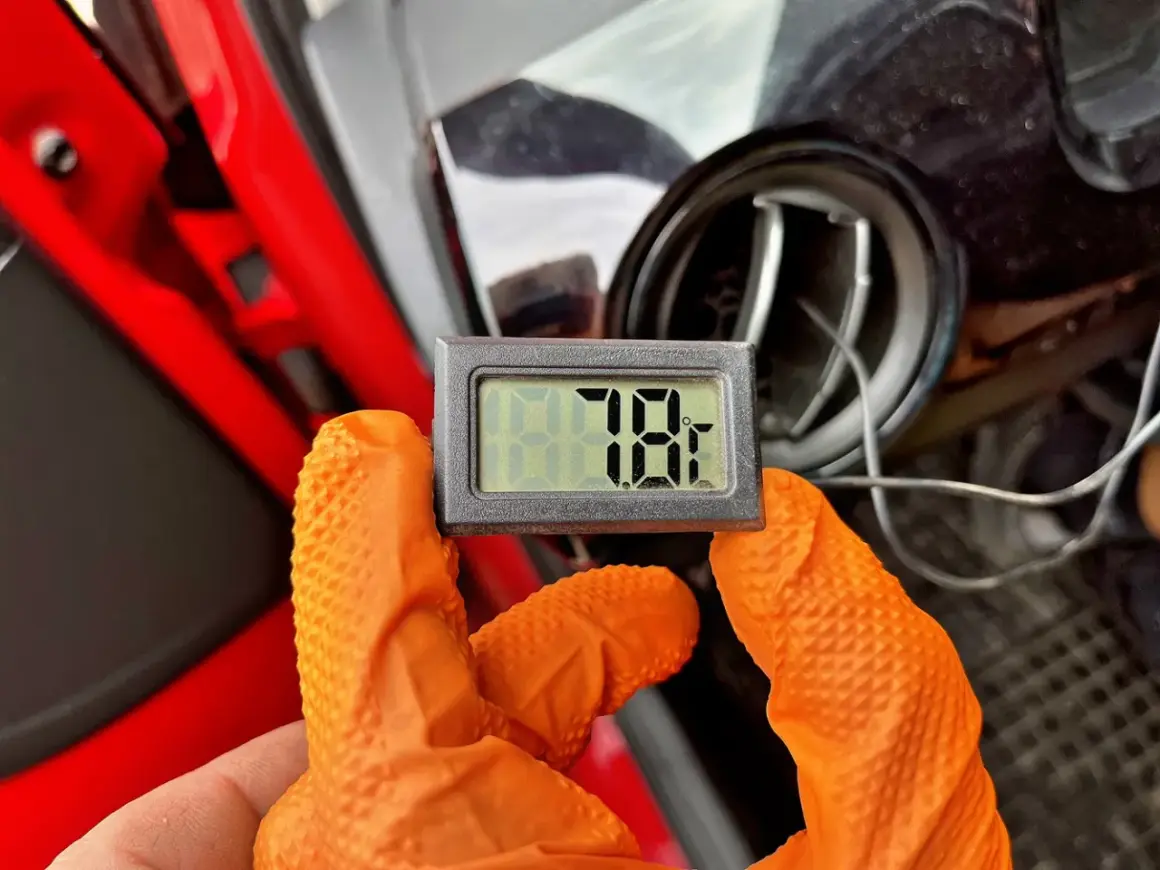 Rękawiczki w kolorze pomarańczowym trzymają termometr pokazujący 78°F. To część samodzielnego nabijania klimatyzacji.