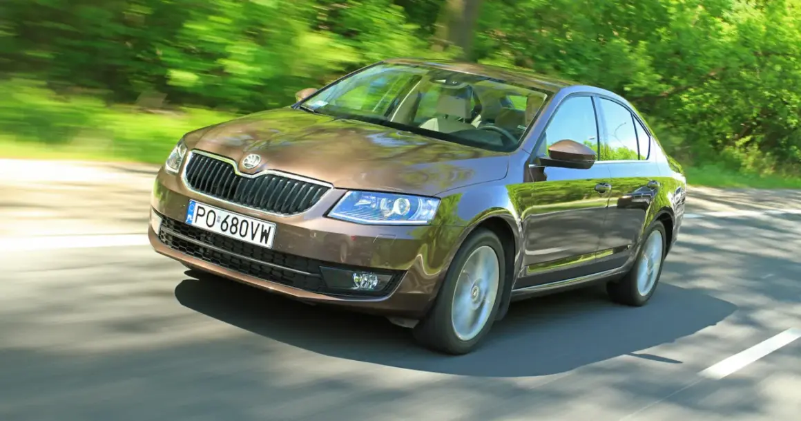 Brązowa Octavia 2.0 TDI pędzi leśną drogą, odbijając zieleń drzew w lśniącej karoserii.