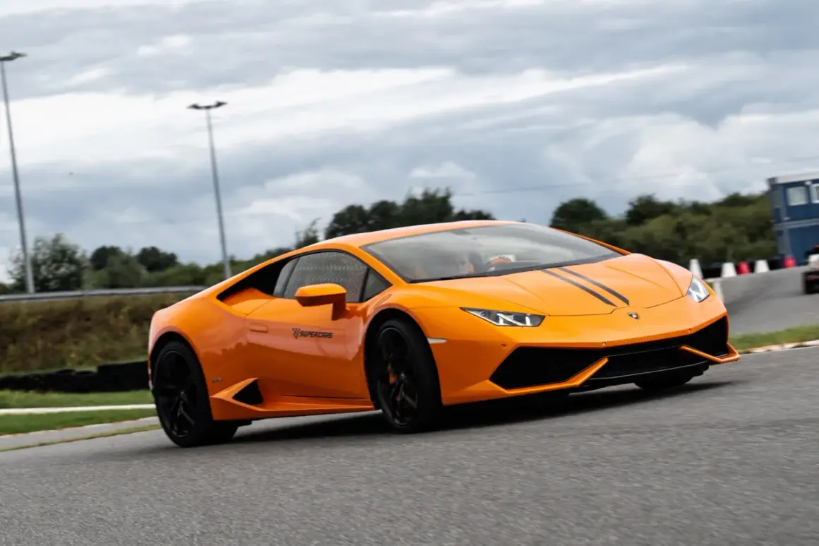 Pomarańczowe Lamborghini z czarnymi pasami na masce podczas szybkiego przejazdu po torze wyścigowym.