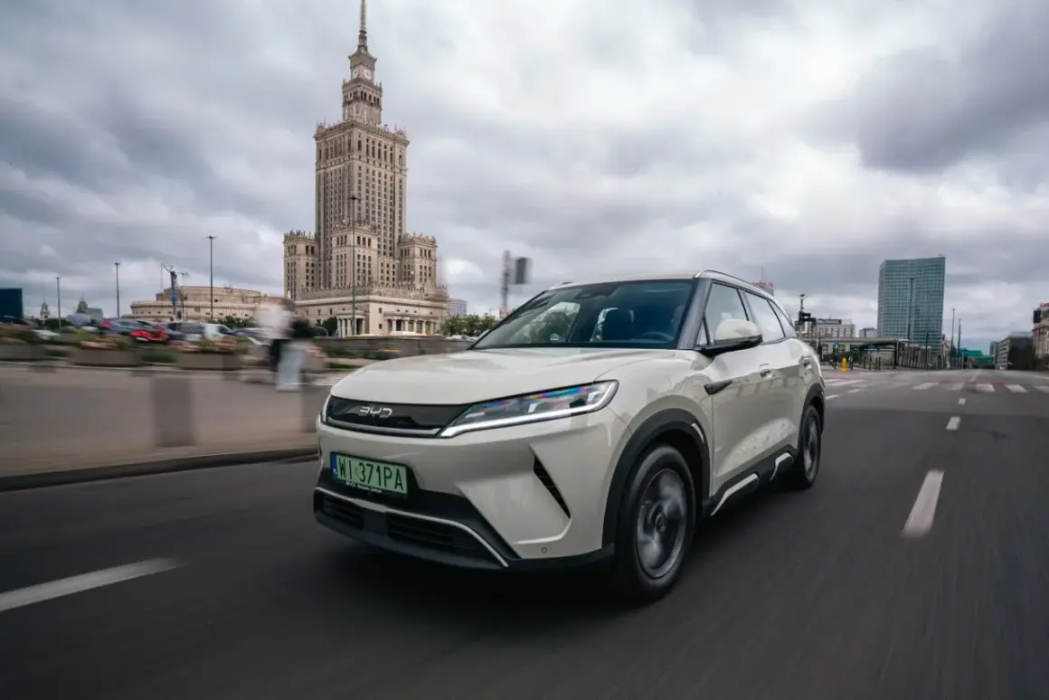 Biały SUV marki BYD, jeden z chińskich marek aut, jedzie ulicą Warszawy. W tle Pałac Kultury i Nauki.