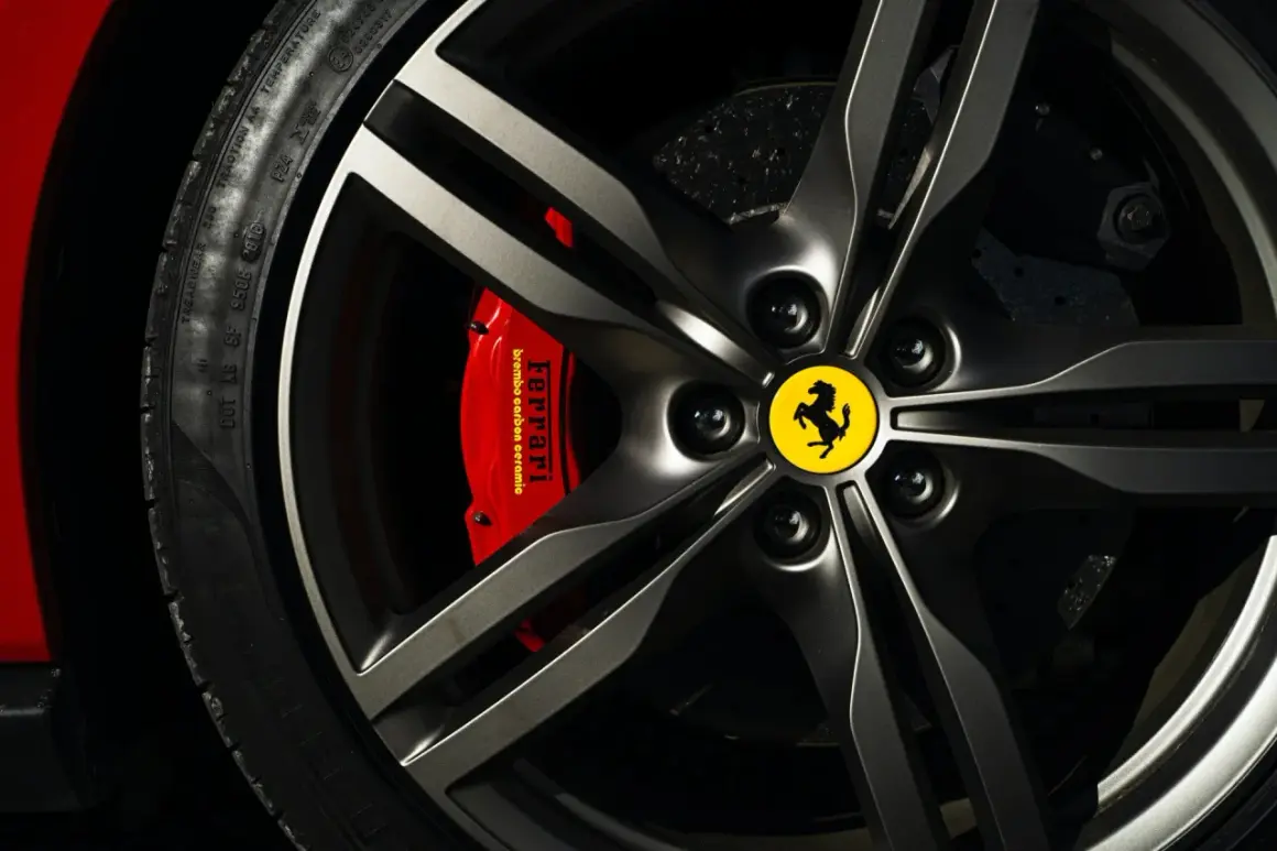 Logo samochodu ze skrzydłami na feldze Ferrari. Czerwony zacisk hamulcowy z napisem "Ferrari".