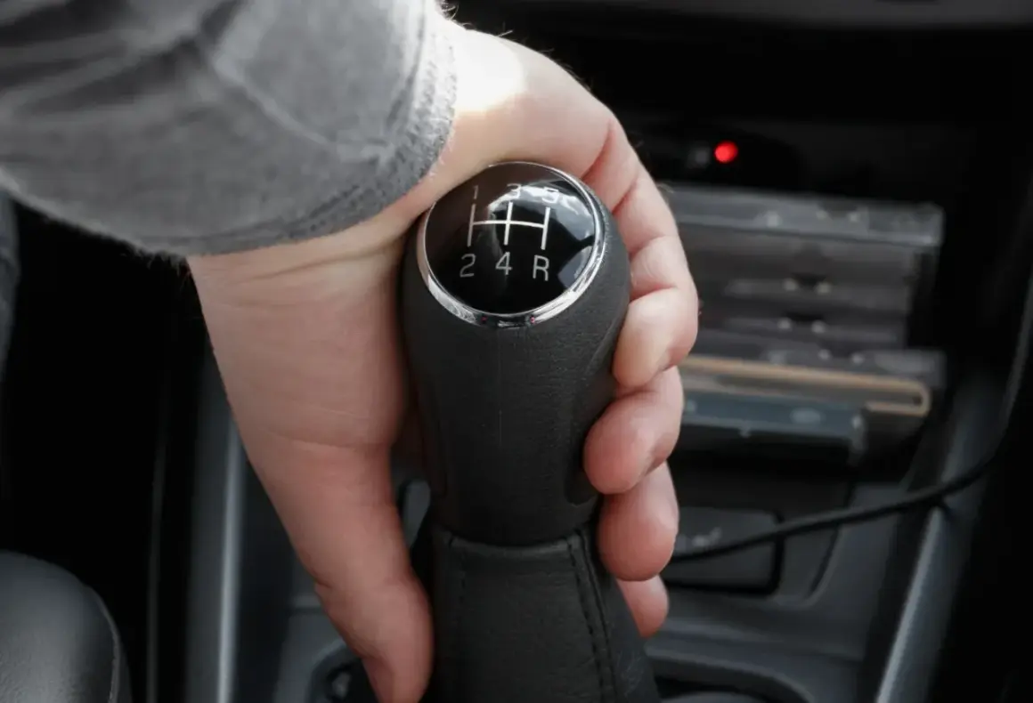 Dłoń chwyta lewarek zmiany biegów, ustawiając go na wsteczny w automacie.