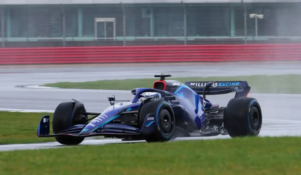 Niebieski bolid Formuły 1 z logo Williams Racing na torze w deszczu. Kierowcy formuły 1 muszą być odważni w takich warunkach.