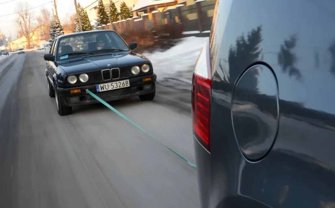 Czarny BMW holowany przez inny samochód, bo zabrakło paliwa. Co zamiast plaka do odpalenia? Lina holownicza!
