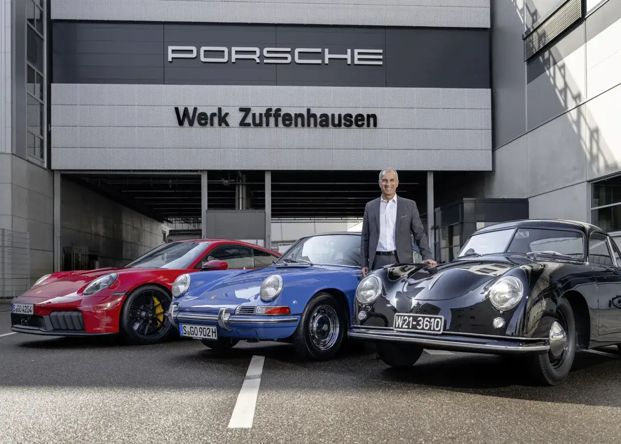 Mężczyzna w garniturze stoi obok trzech Porsche: czerwonego, niebieskiego i czarnego. Porsche to samochody z Niemiec, a ten napis