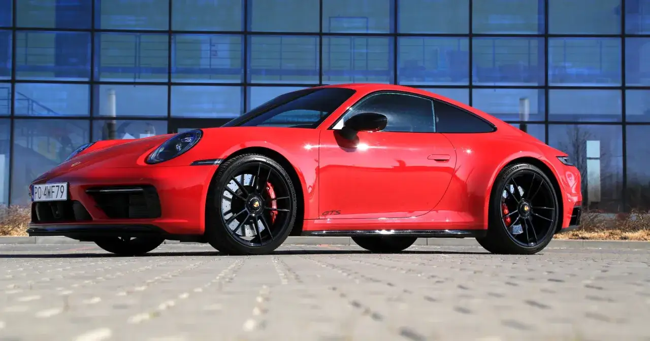 Czerwone Porsche 911 GTS, symbol najmniej awaryjnych aut, lśni na tle nowoczesnego budynku.