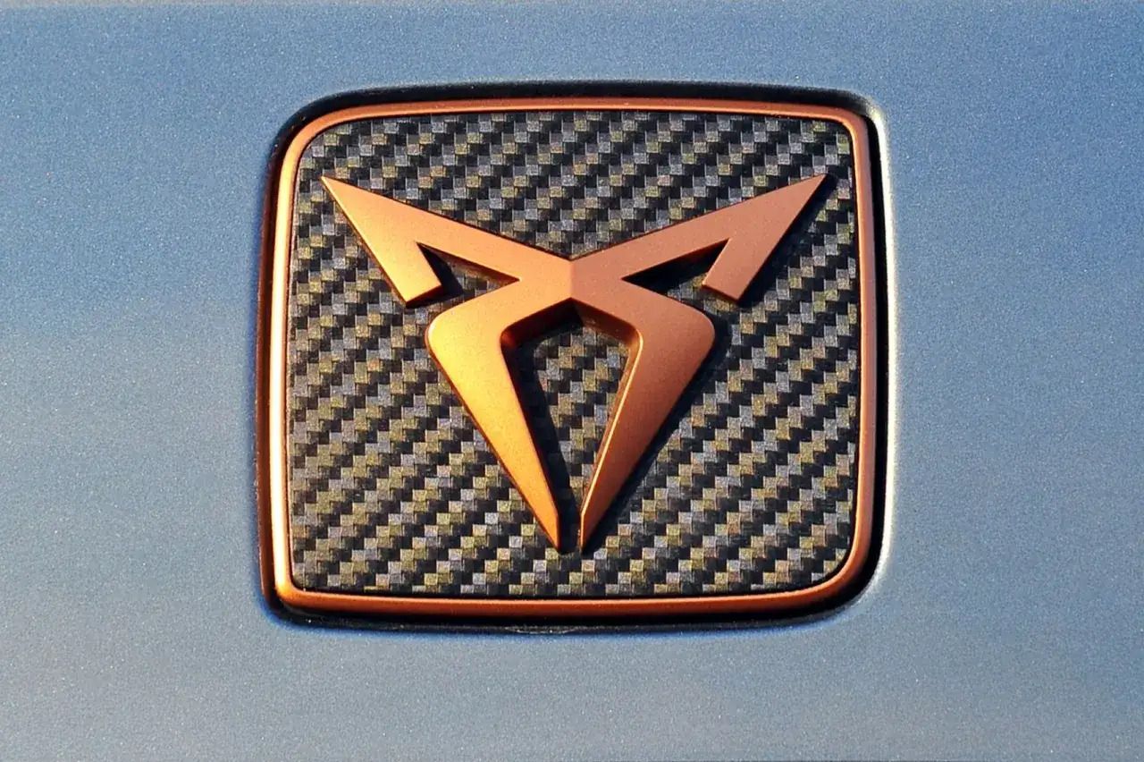 Nowe loga samochod&oacute;w: miedziane logo Cupra na tle wł&oacute;kna węglowego.