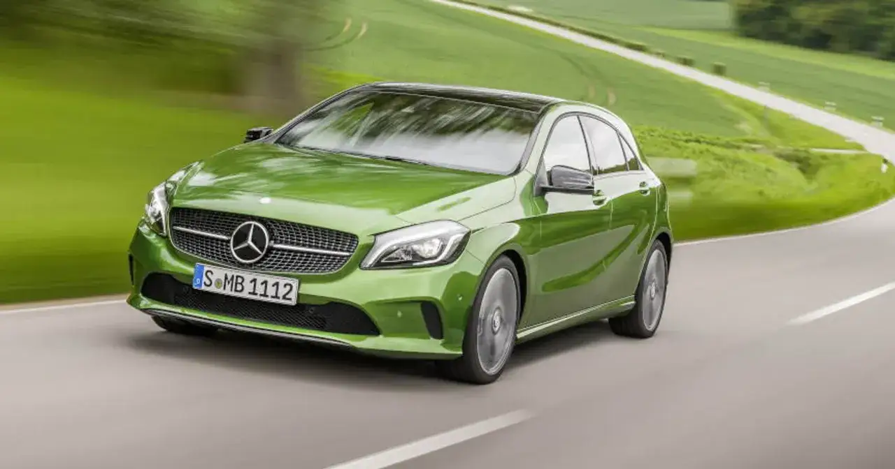 Zielony Mercedes klasy C pędzi po krętej drodze wśr&oacute;d zielonych p&oacute;l.