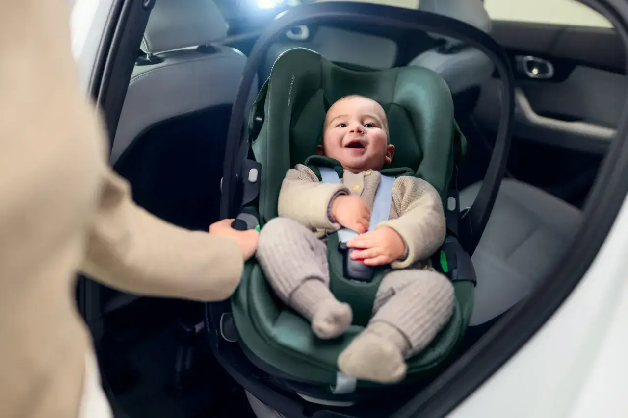 Uśmiechnięte dziecko w zielonym foteliku samochodowym. Czy baza isofix pasuje do każdego fotelika? Sprawdźmy!
