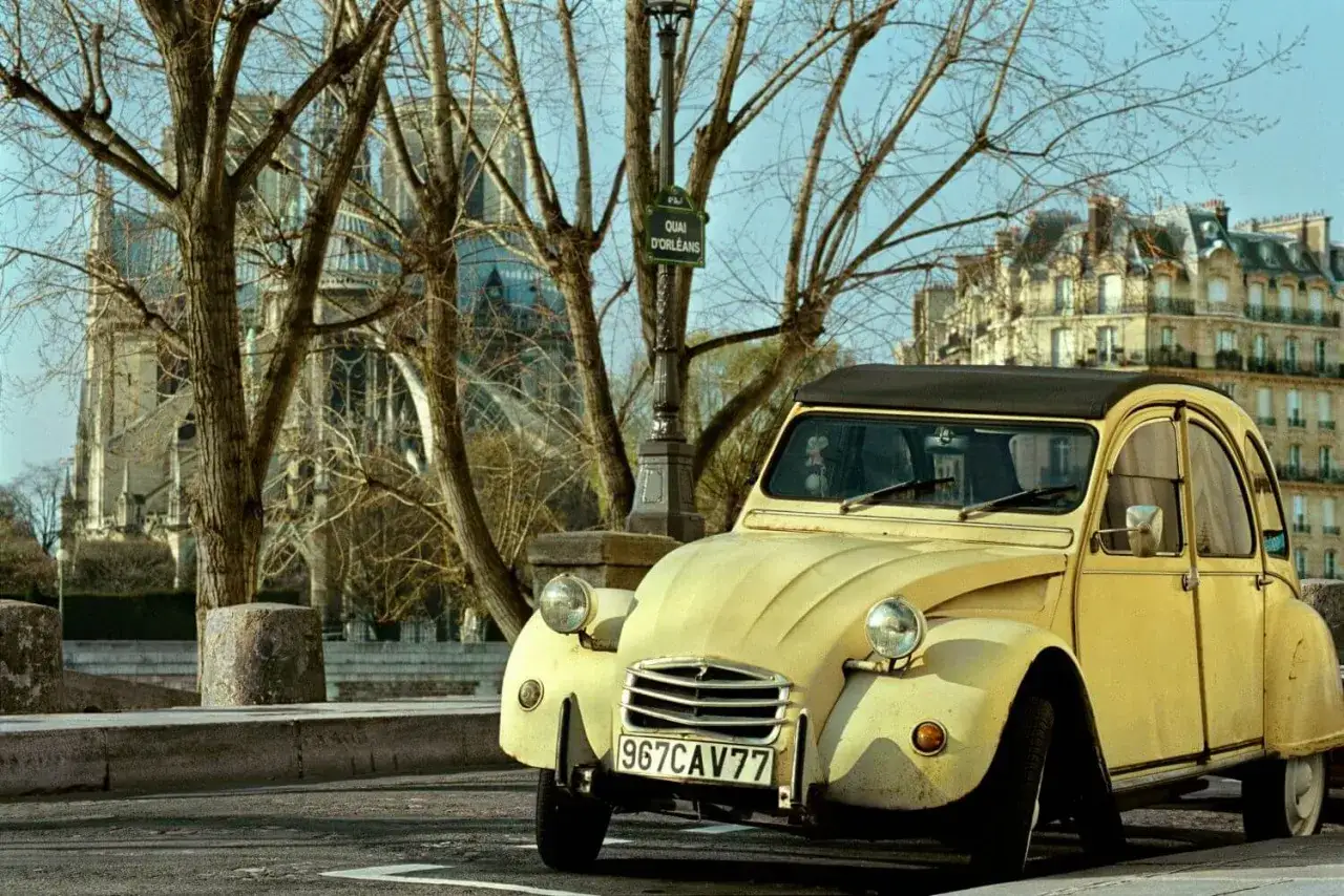 Ż&oacute;łty Citro&euml;n 2CV, ikona francuskich marek samochod&oacute;w, parkuje na tle paryskiej kamienicy i katedry.