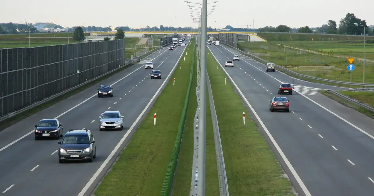 Droga ekspresowa z barierami dźwiękochłonnymi i pasami zieleni, gdzie ruch samochodowy jest mniejszy niż na autostradzie.