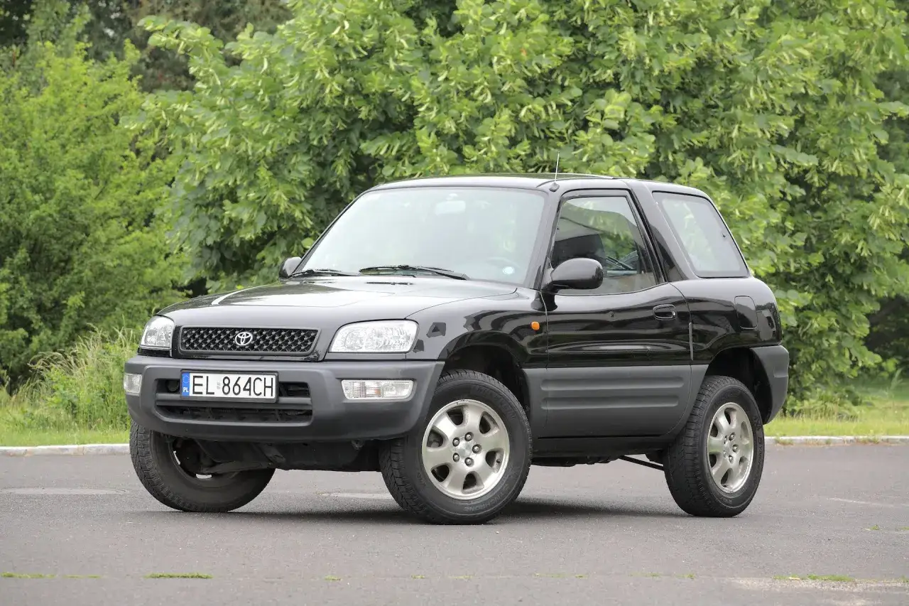 Czarny, 3-drzwiowy SUV Toyota RAV4, jeden z najmniej awaryjnych SUV-&oacute;w 10 letnich, zaparkowany na tle zieleni.