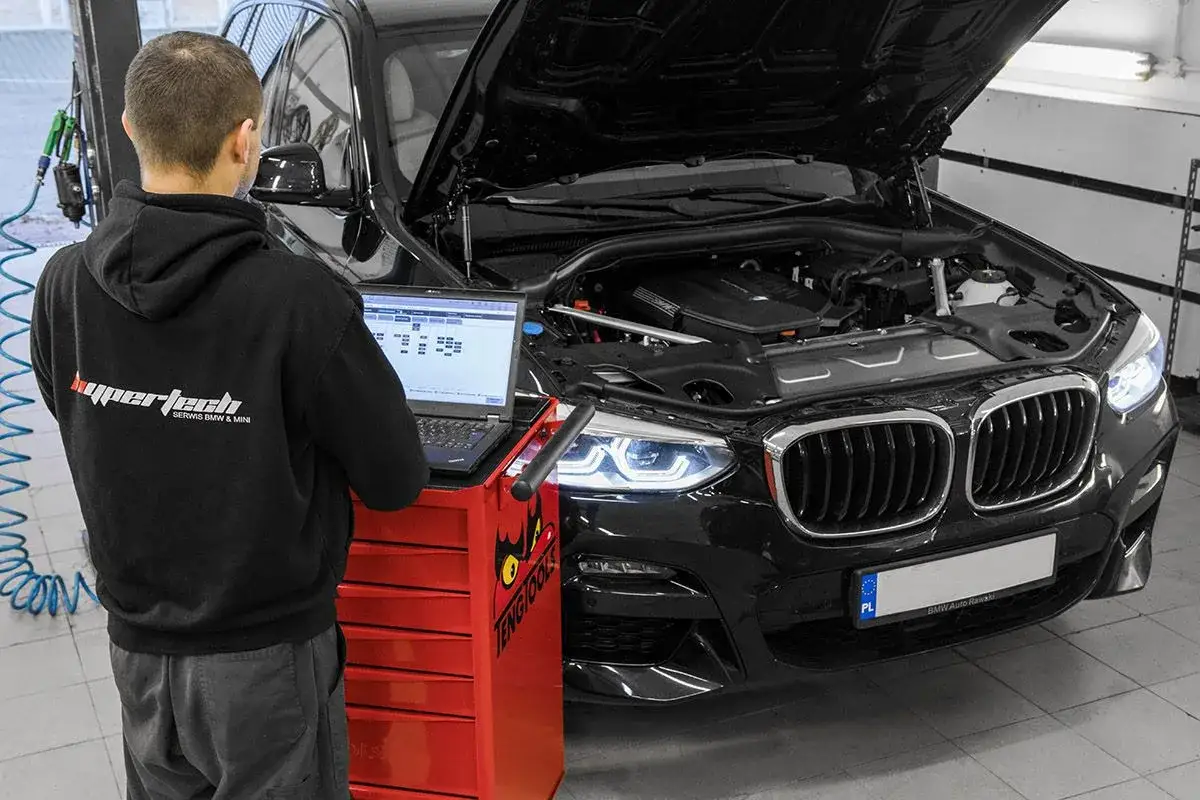 Mechanik diagnozuje BMW, sprawdzając, czy BMW jest drogie w utrzymaniu. Pod maską silnik, na laptopie dane diagnostyczne.