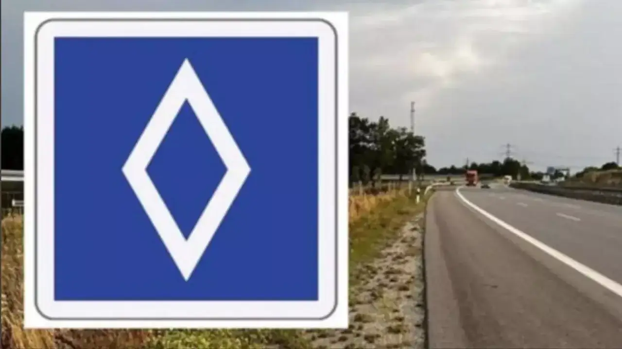 Znak drogowy: biały romb na niebieskim tle. Obok autostrada z ruchem.