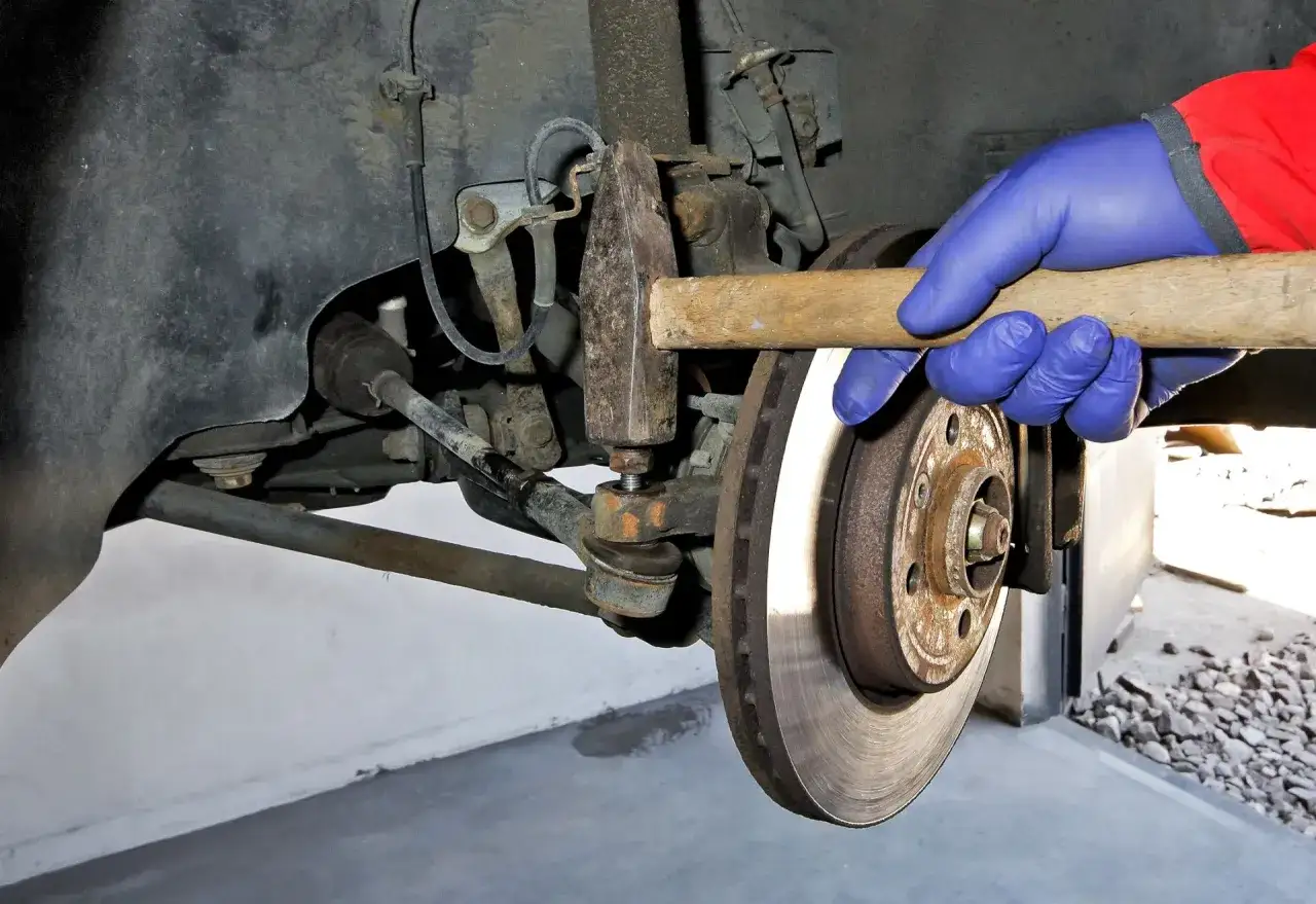 Mechanik w niebieskiej rękawiczce używa młotka do wymiany końcówek drążków kierowniczych w samochodzie.