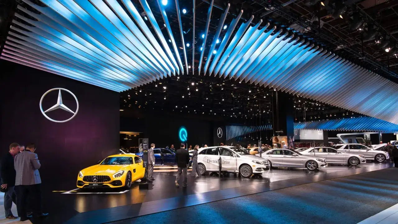 Na wystawie motoryzacyjnej prezentowane są luksusowe marki samochodów, w tym żółty Mercedes-AMG GT S i srebrne modele z napędem elektrycznym.