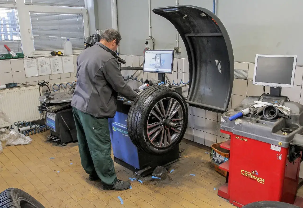 Mechanik przy maszynie do wyważania kół. Sprawdza parametry na ekranie, przygotowując się do sezonowej wymiany opon.