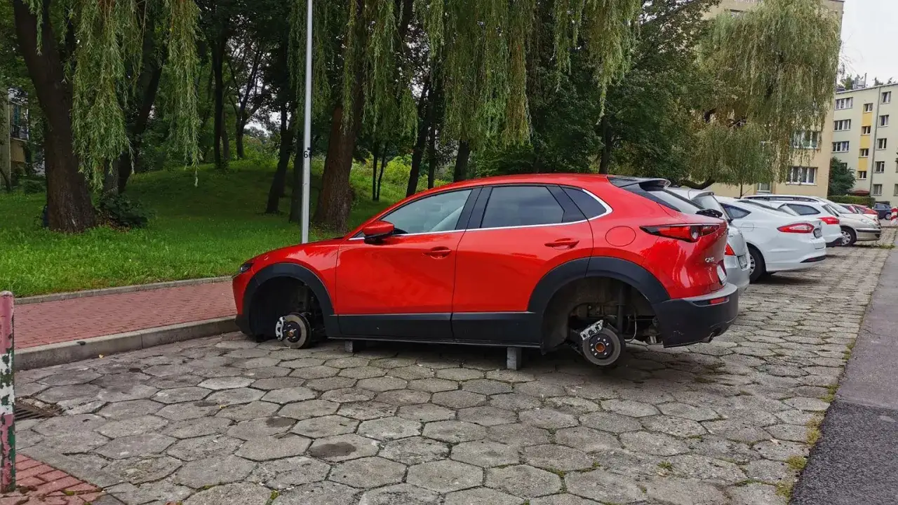 Czerwona Mazda bez k&oacute;ł, stojąca na cegłach. Wygląda jak jeden z najczęściej kradzionych aut, pozbawiony k&oacute;ł.