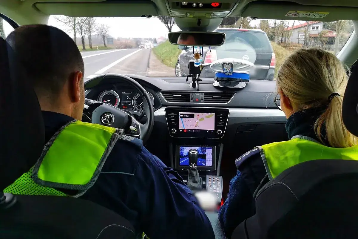 Policjanci w radiowozie, jadący drogą. Czy trzeba mieć prawo jazdy przy sobie? Zapytaj funkcjonariusza.