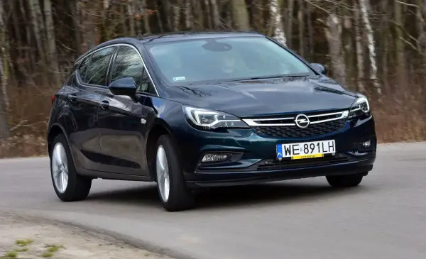 Ciemnozielona Astra K 1.6 CDTI w ruchu, z widocznym kierowcą za kierownicą, na tle lasu.