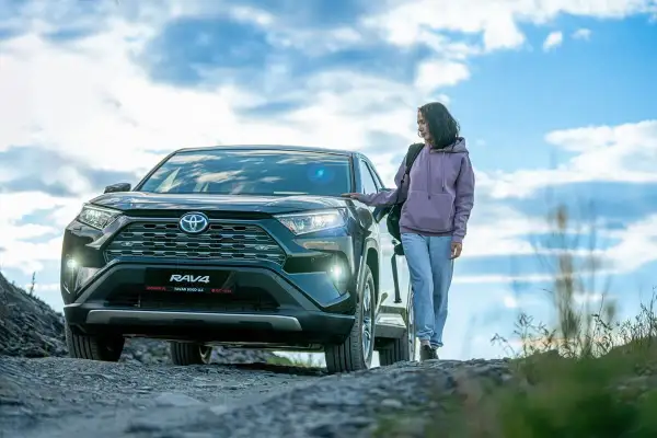 Kobieta obok Toyoty RAV4, jednego z najmniej awaryjnych crossoverów, na tle nieba z chmurami.