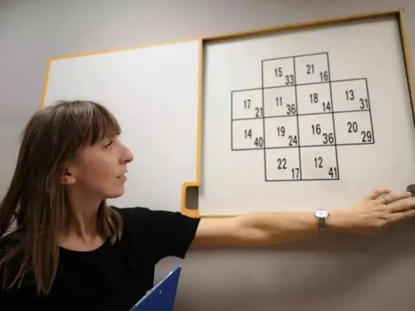 Kobieta podczas testów psychologicznych dla kierowców, wskazująca na tablicę z liczbami.