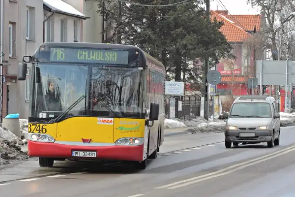 Żółto-czerwony autobus miejski linii 716 jedzie po mokrej drodze. Czy autobus ma pierwszeństwo? Obok jedzie srebrny van.