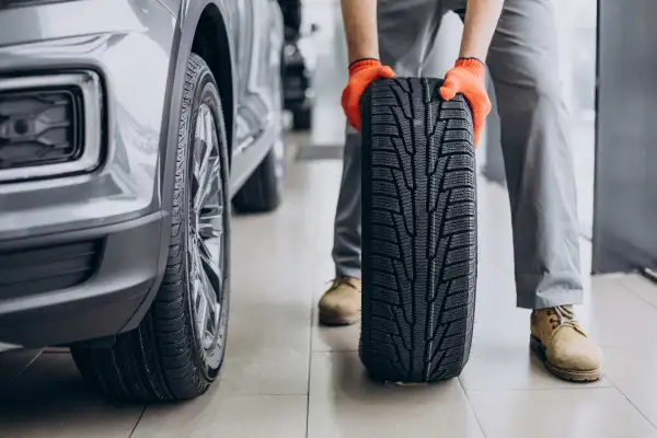 Mechanik w pomarańczowych rękawiczkach trzyma nowe opony letnie obok samochodu. Czas na test opon letnich!