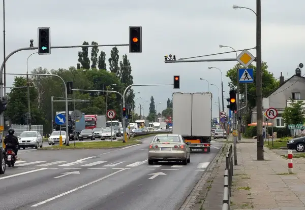 Kierowca srebrnego sedana decyduje się na przejazd na żółtym świetle, mimo że sygnalizator obok świeci na czerwono.