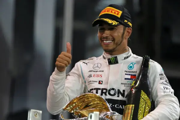 Lewis Hamilton, jeden z najlepsi kierowcy f1, świętuje zwycięstwo z pucharem i szampanem, pokazując kciuk w górę.