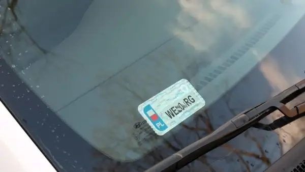 Naklejki na samochód, w tym obowiązkowe naklejki z numerem rejestracyjnym, umieszczone na przedniej szybie.