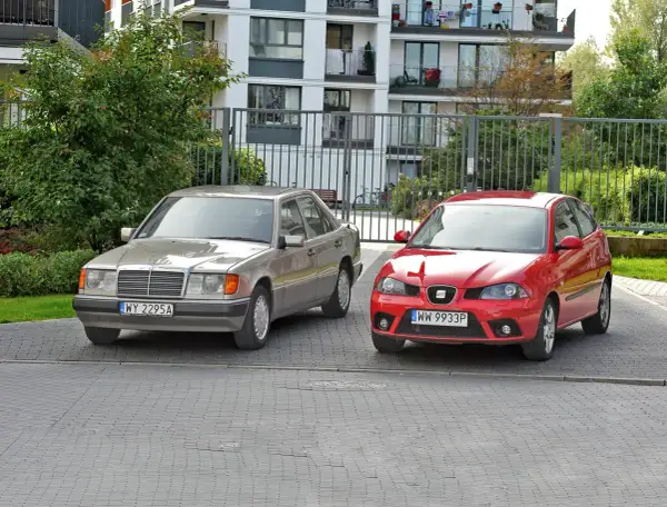 Dwa samochody, srebrny Mercedes i czerwony Seat, stoją obok siebie. To tylko mała część rosnącej ilości samochodów w Polsce.