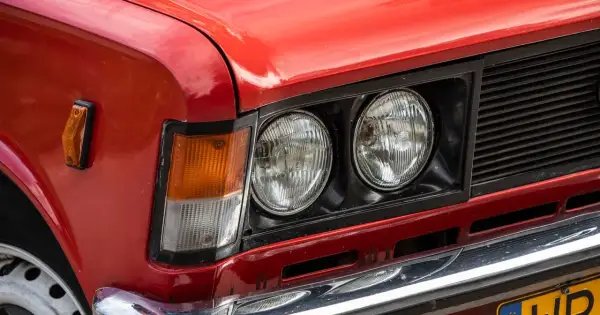 Czerwone auto z włoch, z podwójnymi okrągłymi reflektorami i pomarańczowym kierunkowskazem.