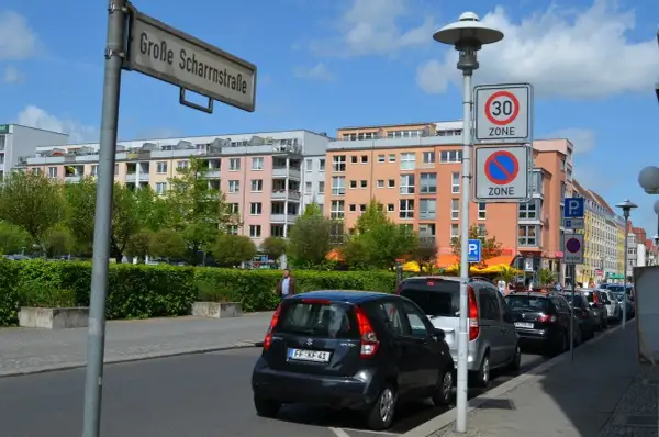 Ulica w Niemczech z kolorowymi kamienicami, znakami drogowymi (w tym fotoradary w niemczech) i zaparkowanymi samochodami.