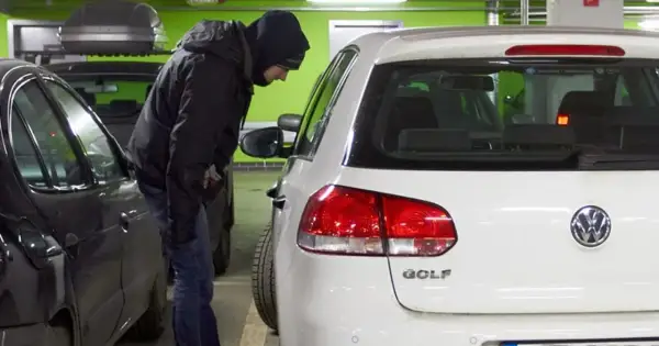 Mężczyzna w kapturze pochyla się nad białym Volkswagenem Golfem, jednym z najczęściej kradzionych aut.